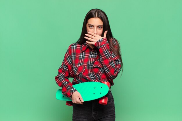 Young pretty woman covering mouth with hands with a shocked, surprised expression, keeping a secret or saying oops. skate board concept