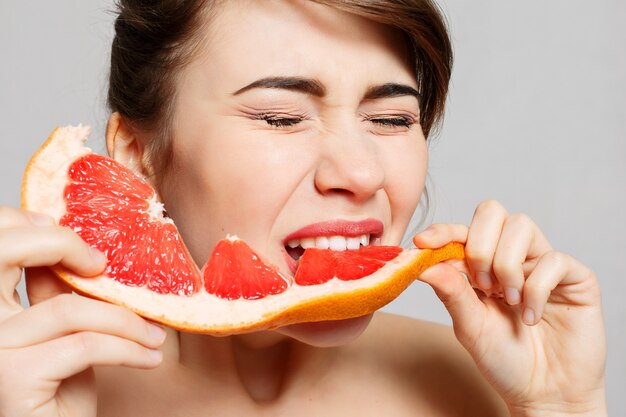 La giovane donna graziosa o la ragazza sexy sveglia con capelli lunghi tiene la fetta della frutta del pompelmo,