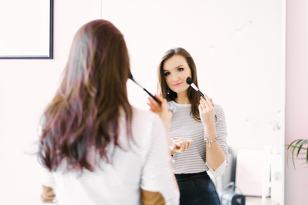 Молодая красивая женщина делает макияж дома, глядя в зеркало