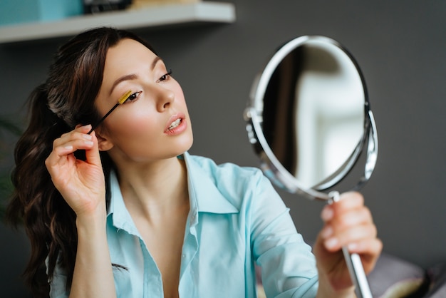 Young pretty woman does makeup at home while looking in the mirror