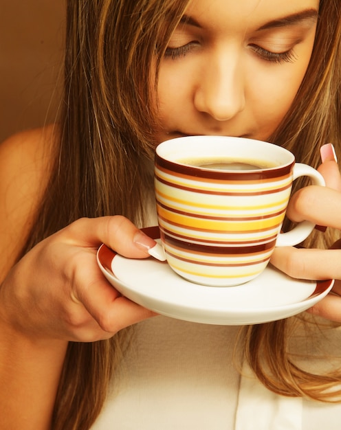 Young pretty woman drinking coffee over beige background