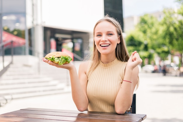 Foto giovane bella donna che mangia hamburger all'aperto per strada