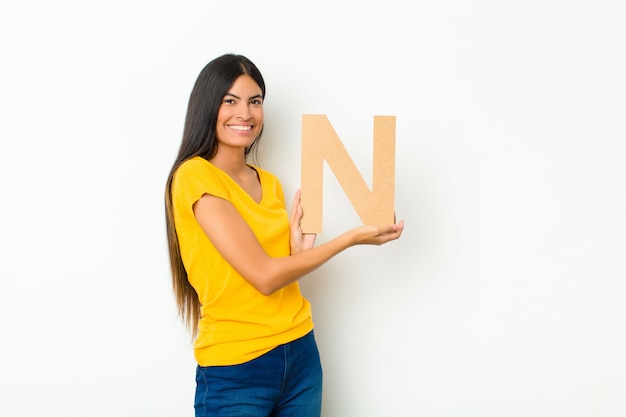Молодая симпатичная женщина возбуждена, счастлива, радостна, держит букву N алфавита, чтобы образовать слово или предложение.