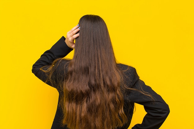 Giovane bella donna sentirsi senza sensi e confuso, pensando a una soluzione, con la mano sull'anca e altro sulla testa, lavoro di retrovisione o concetto di affari