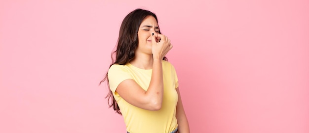 young pretty woman feeling disgusted, holding nose to avoid smelling a foul and unpleasant stench