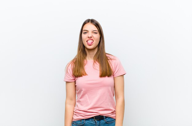 Young pretty woman feeling disgusted and irritated, sticking tongue out, disliking something nasty and yucky against white background