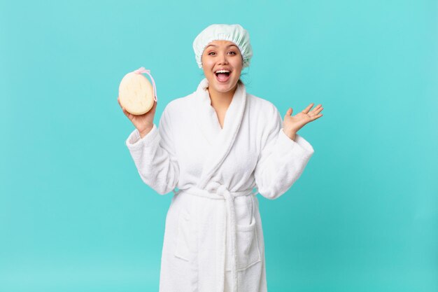 Young pretty woman feeling happy and astonished at something unbelievable and wearing bath robe after shower