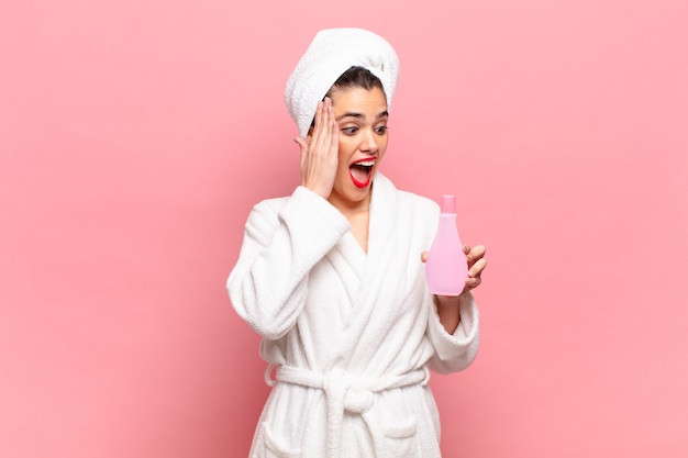 Young pretty woman feeling happy, excited and surprised, looking to the side with both hands on face. bathrobe and face cleaning concept