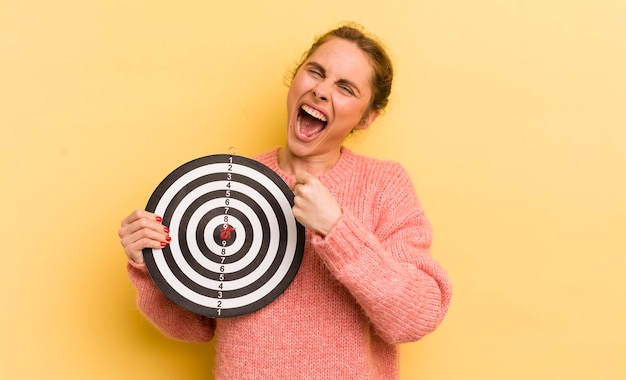 Young pretty woman feeling happy and facing a challenge or celebrating dart target concept