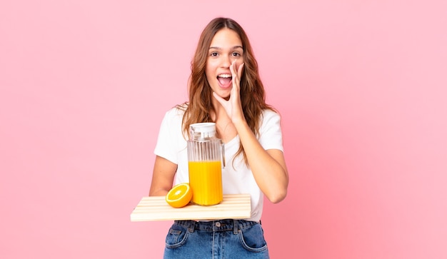 Young pretty woman feeling happy,giving a big shout out with hands next to mouth and holding a tray with an orange juice