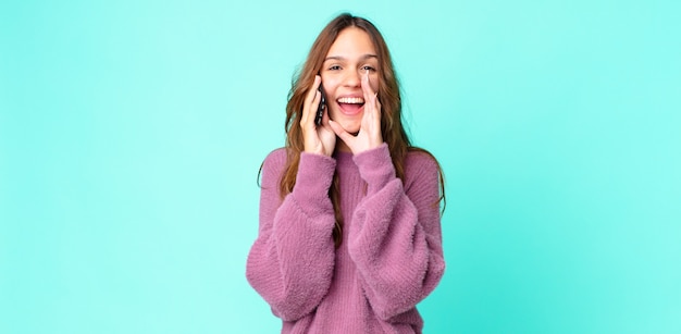 Young pretty woman feeling happy,giving a big shout out with hands next to mouth and using a smartphone