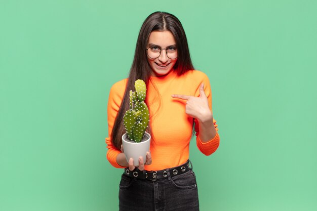 Young pretty woman feeling happy, surprised and proud, pointing to self with an excited, amazed look. cactus concept