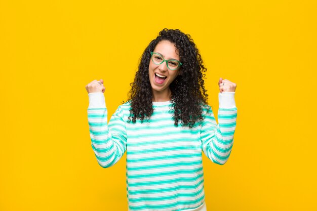 Young pretty woman feeling happy, surprised and proud, shouting and celebrating success with a big smile against orange wall