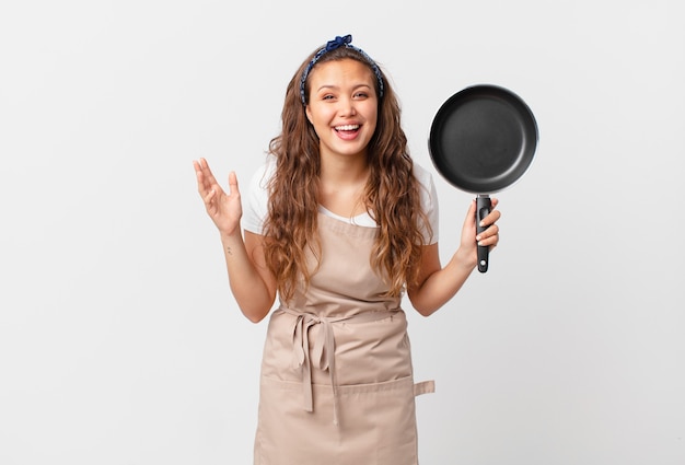 Giovane bella donna che si sente felice, sorpresa di realizzare una soluzione o un'idea del concetto di chef e con in mano una padella