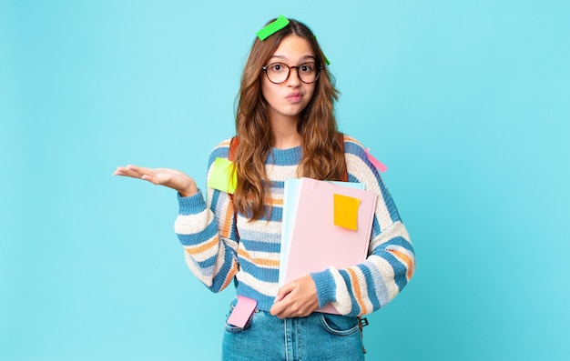 Giovane bella donna che si sente perplessa e confusa e dubita di una borsa e tiene in mano dei libri