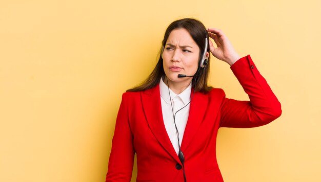 Young pretty woman feeling puzzled and confused scratching head telemarketer concept