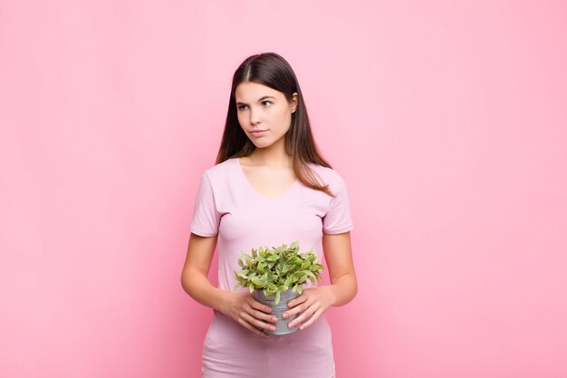 Young pretty woman feeling sad, upset or angry and looking to the side with a negative attitude, frowning in disagreement with a plant