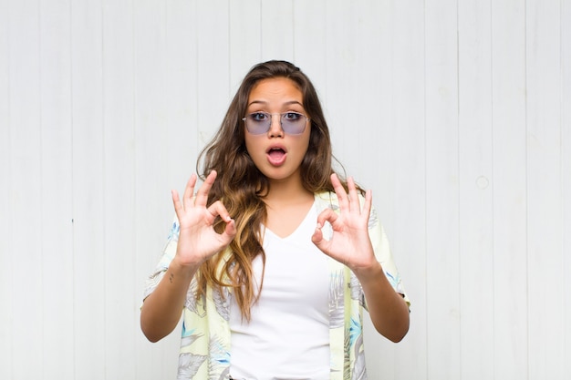 Foto giovane donna graziosa che si sente scioccata, stupita e sorpresa, mostrando approvazione facendo segno ok con entrambe le mani