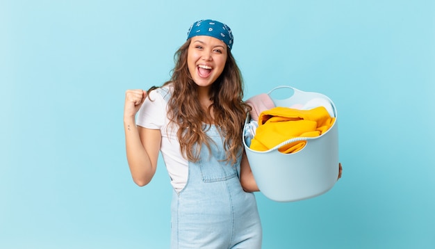 Young pretty woman feeling shocked,laughing and celebrating success and holding a wash clothes basket