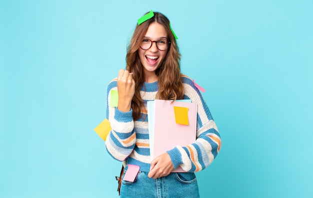 Young pretty woman feeling shocked,laughing and celebrating success with a bag and holding books