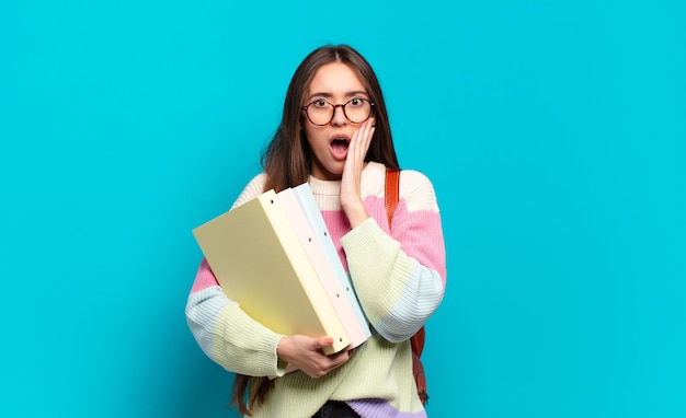 Young pretty woman feeling shocked and scared, looking terrified with open mouth and hands on cheeks