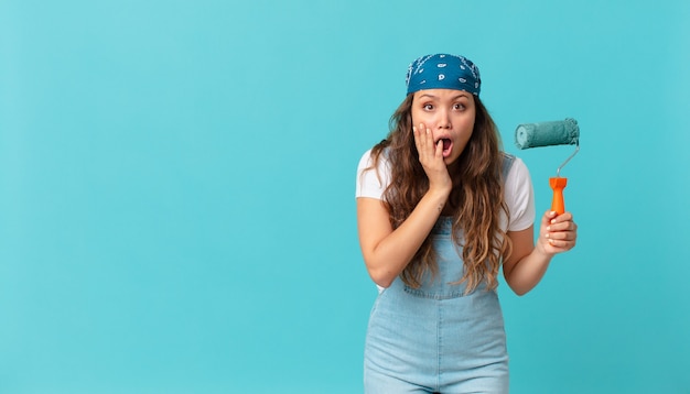 Young pretty woman feeling shocked and scared and painting a wall