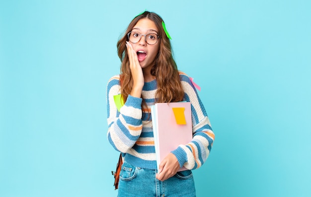 Young pretty woman feeling shocked and scared with a bag and holding books