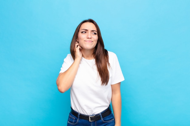 Young pretty woman feeling stressed, frustrated and tired, rubbing painful neck, with a worried, troubled look against blue wall