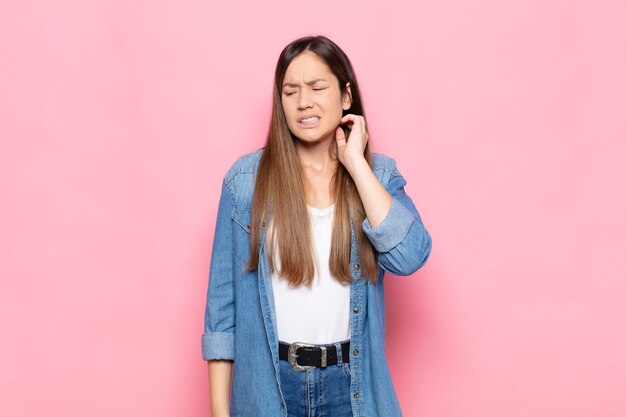 Young pretty woman feeling stressed, frustrated and tired, rubbing painful neck, with a worried, troubled look