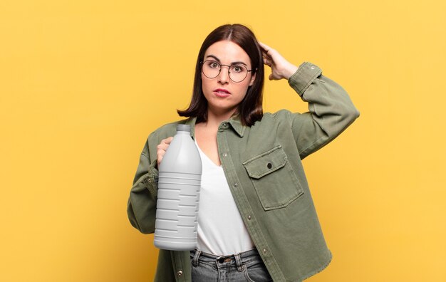 Young pretty woman feeling stressed holding a cleaning product bottle