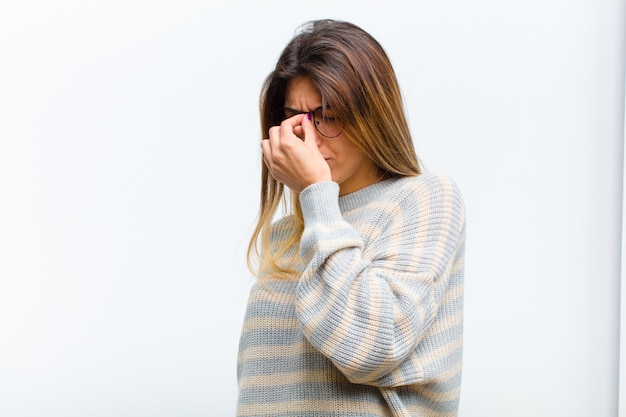 Giovane bella donna sentirsi stressata, infelice e frustrata, toccando la fronte e soffrendo di emicrania di forte mal di testa contro il muro bianco