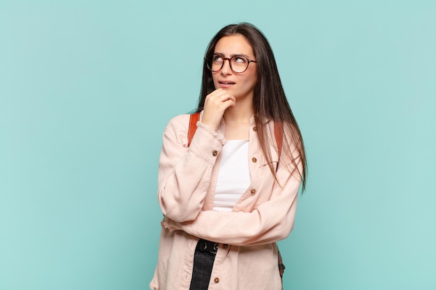 Giovane bella donna che si sente premurosa, si chiede o immagina idee, sogna ad occhi aperti e alza lo sguardo per copiare lo spazio. concetto di studente