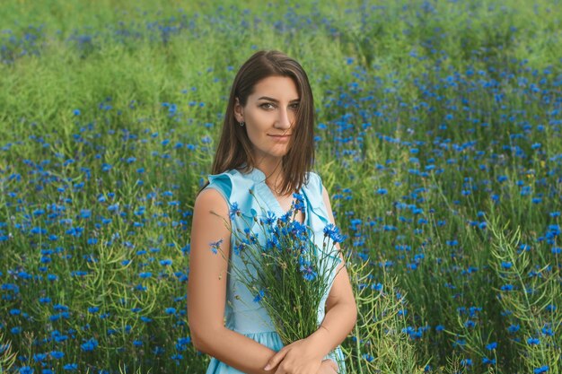 Young pretty woman among the field of beautiful cornflowers