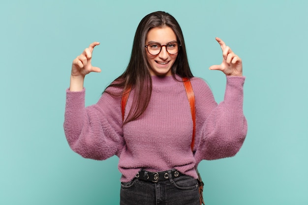 Young pretty woman framing or outlining own smile with both hands, looking positive and happy