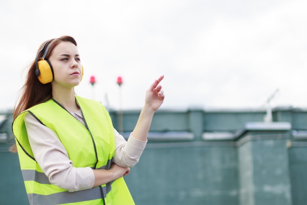 Young pretty woman in green west and earmuffs stand on roof, hold tablet