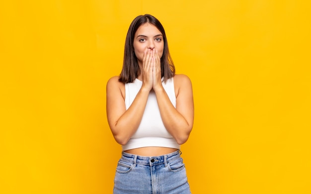 Young pretty woman happy and excited, surprised and amazed covering mouth with hands, giggling with a cute expression