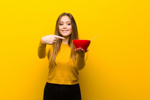 オレンジ色の壁に対して朝食を持っている若いきれいな女性