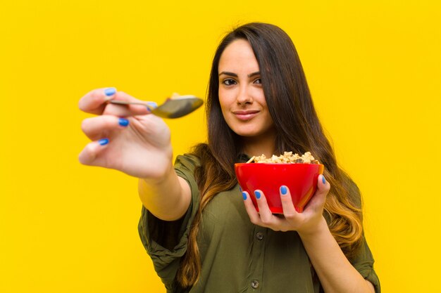 Young pretty woman having breakfast against orange wall