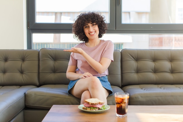 Young pretty woman having a sandwich sitting on a sofa at home