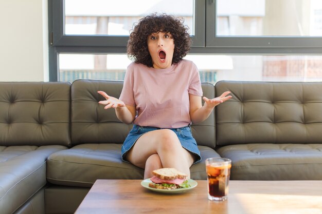 Photo young pretty woman having a sandwich sitting on a sofa at home