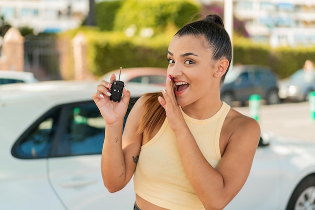 Young pretty woman holding car keys at outdoors whispering something