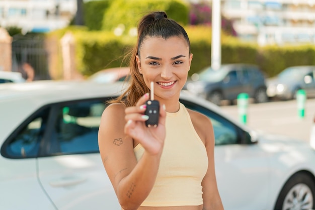 幸せな表情で外で車の鍵を握っている美しい若い女性