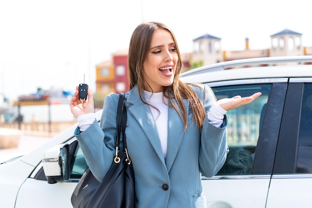 驚きの表情で屋外で車のキーを保持している若いきれいな女性