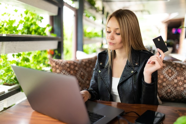 Giovane donna graziosa che tiene la carta di credito e utilizza il computer portatile. concetto di acquisto online