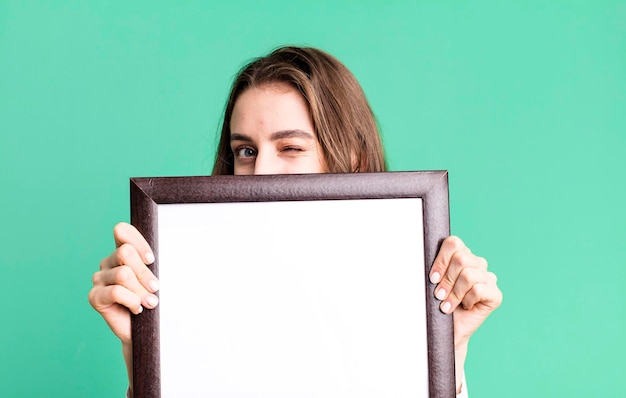 Young pretty woman holding an empty frame copy space