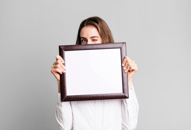 Photo young pretty woman holding an empty frame copy space