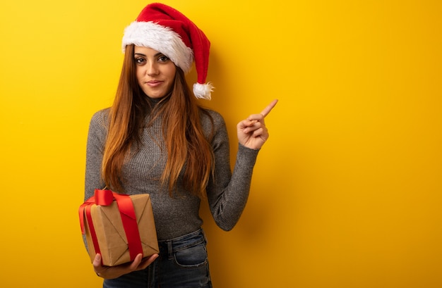 Young pretty woman holding gift smiling and pointing to the side