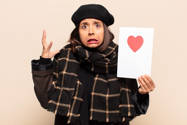 Young pretty woman holding a heart card making a face