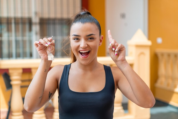 Young pretty woman holding home keys at outdoors pointing up a great idea