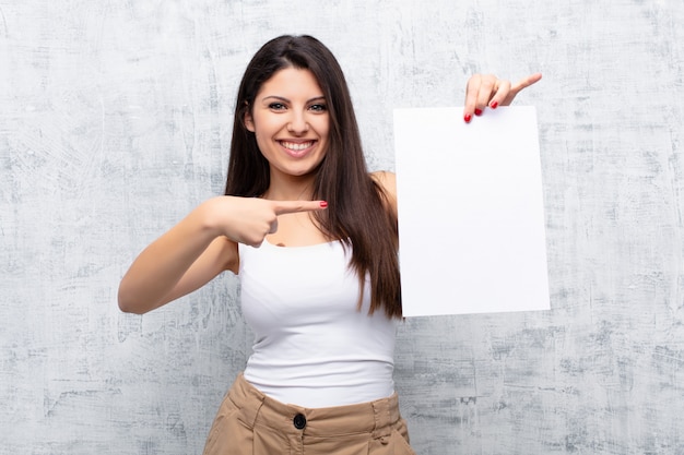 Young pretty woman holding a paper sheet against grunge cement wall